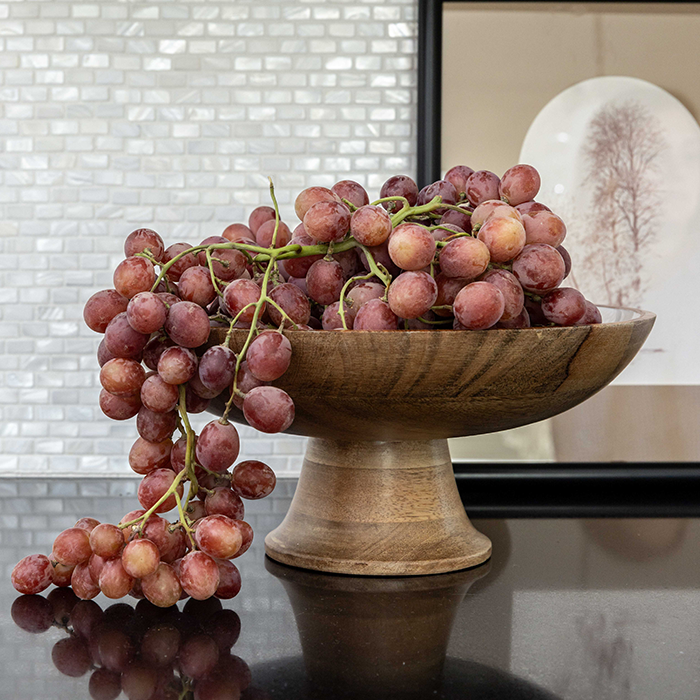 Grapes flowing out of a wooden bowl on a kitchen backsplash.