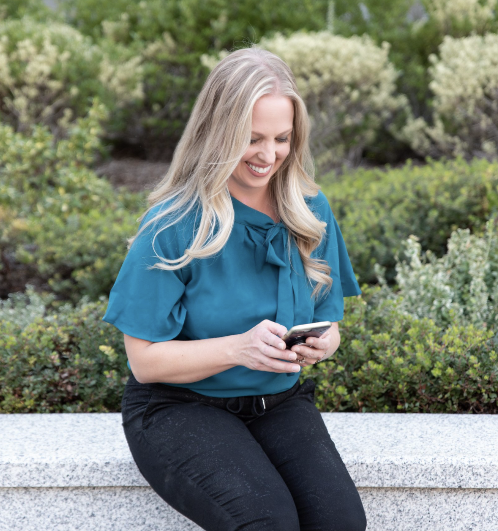 Rebecca sitting on a bench smiling at her phone